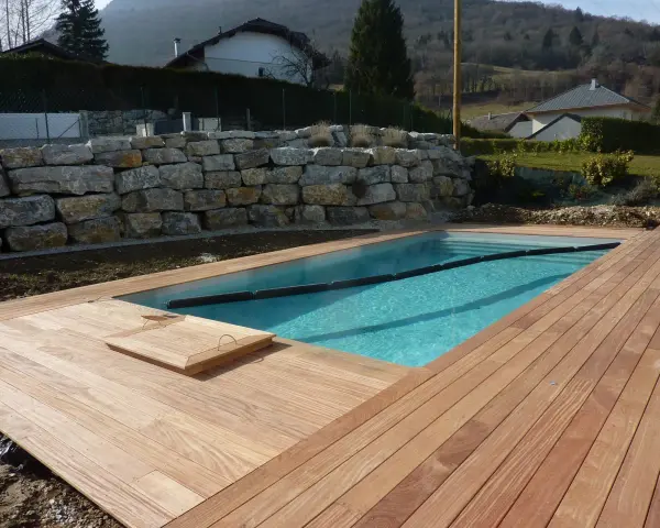 Piscine en bois avec terrasse en bois, mur de soutènement en pierre. Entretien piscine bois facile avec cette belle installation.