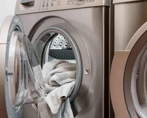 Machine à laver avec une porte ouverte, remplie de linge gris. Choisir la lessive la moins toxique pour un lavage sain.