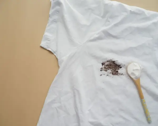 Tache sur t-shirt blanc après lavage, avec une cuillère de poudre blanche à côté.
