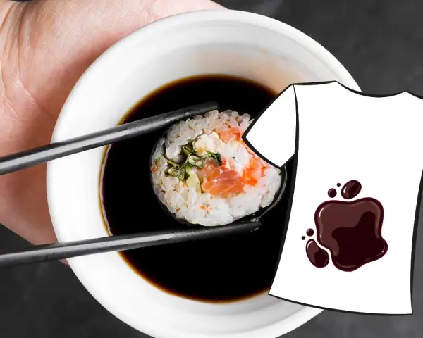 Une main tient une pince à sushi trempant un rouleau dans une sauce soja. Une tache de sauce soja est dessinée sur un t-shirt blanc.