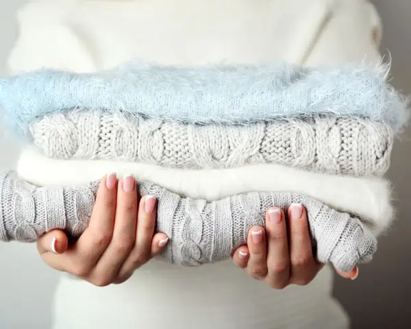 Pile de pulls en laine douce, gris et blanc, avec un pull bleu ciel. Idéal pour savoir comment detacher un pull blanc et le garder comme neuf.