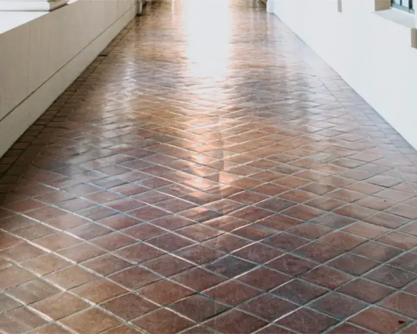 Un couloir avec un carrelage en terre cuite, dont la surface semble avoir été traitée pour vitrifier un carrelage, reflète la lumière.