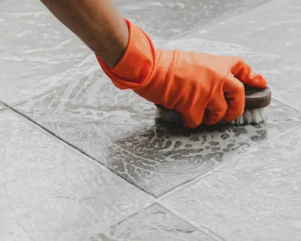Main tenant, ganté, frotte le sol carrelé avec une brosse pour nettoyer le ciment sec.