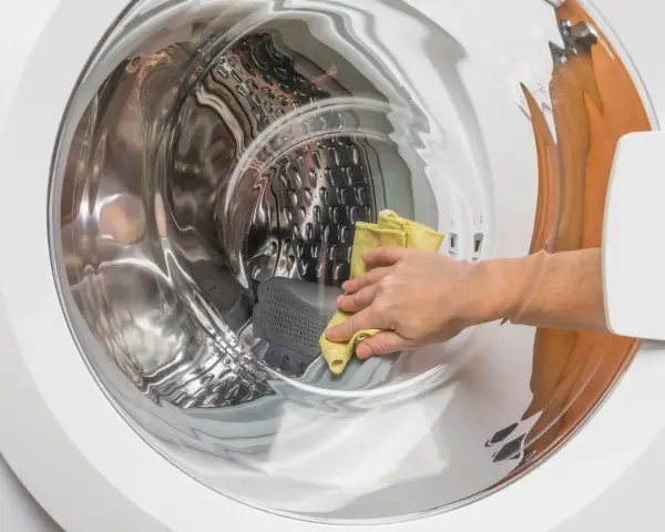 Main d'une personne utilisant un chiffon jaune pour nettoyer l'intérieur d'une machine à laver, une méthode naturelle pour nettoyer machine a laver vinaigre.