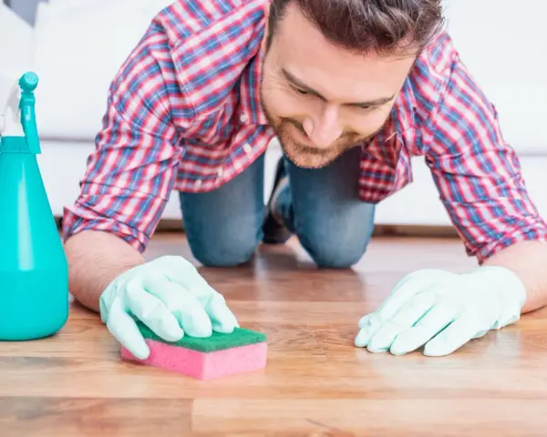 Un homme, muni de gants et d'une éponge, s'agenouille pour nettoyer une tache sur le parquet.