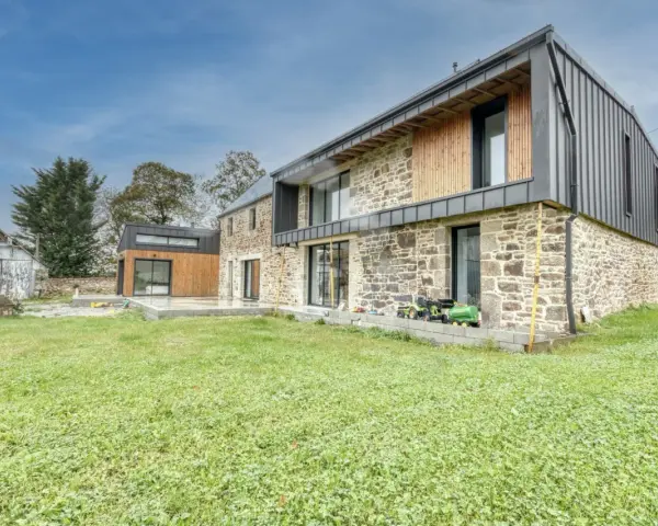 Une maison en pierre rénovée, mêlant tradition et modernité avec des touches de bois et de métal. Un jardin verdoyant entoure cette demeure.