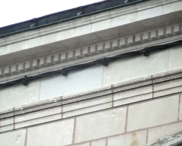 Détail d'une façade en tuffeau avec des câbles noirs fixés. L'image montre comment poncer du tuffeau pour restaurer sa surface.