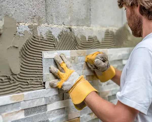Pose de pierre de parement en quinconce. Un artisan pose des pierres naturelles sur un mur avec du mortier.