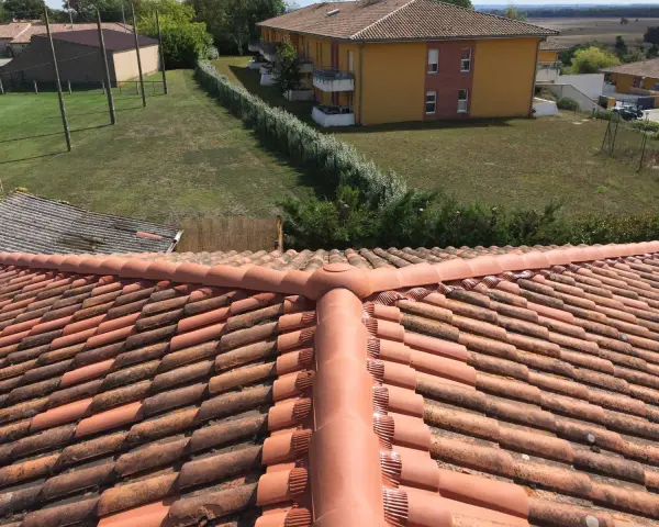Vue aérienne d'un toit en tuiles rouges, avec des bâtiments et de la verdure en arrière-plan. Faut-il imperméabiliser les tuiles pour les protéger ?