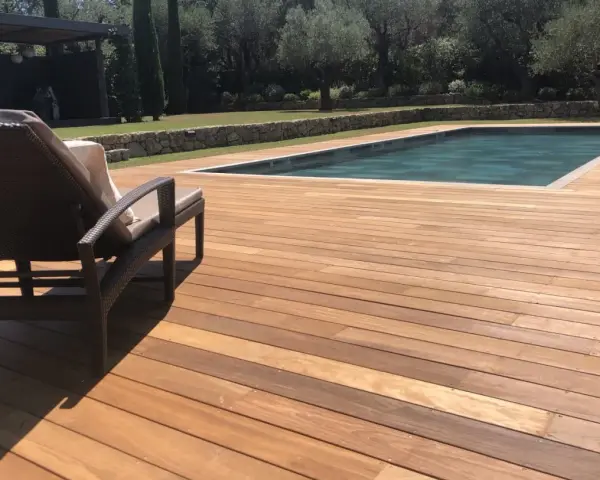 Terrasse en bois d'Ipe, baignée de soleil, avec une chaise longue invitant à la détente près de la piscine.