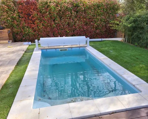 Piscine en béton avec des taches noires sur le fond, entourée de gazon et d'une haie.