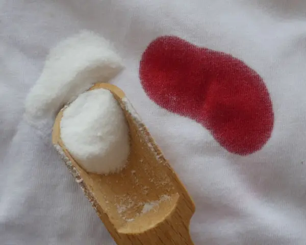 Poudre blanche sur tissu blanc à côté d'une tache rouge. Astuce pour savoir comment enlever des taches de sang sur du coton.