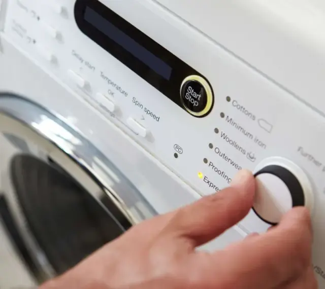 Main d'une personne réglant la température de lavage d'une couette sur un panneau de commande de machine à laver.
