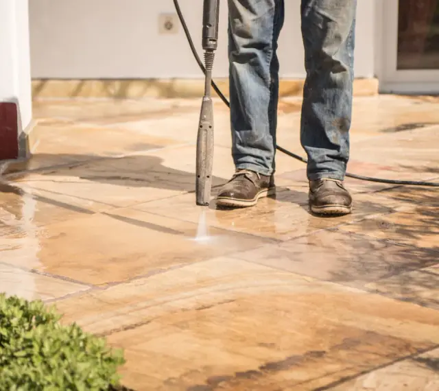 Nettoyer carrelage extérieur noirci avec un nettoyeur haute pression. L'eau projetée révèle la beauté naturelle des dalles.