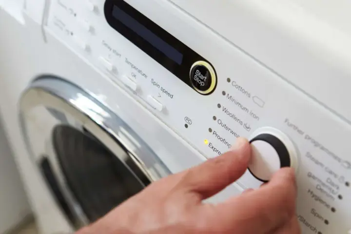 Main d'une personne réglant la température de lavage d'une couette sur un panneau de commande de machine à laver.