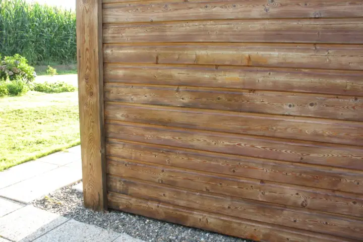 Bardage en bois de mélèze, traité pour l'extérieur, avec un poteau vertical. Le bois présente des nœuds et un grain prononcé.