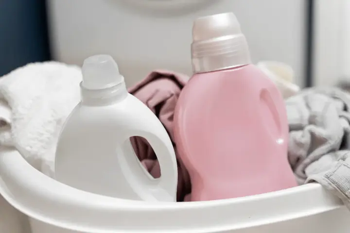 Deux bouteilles de lessive, une blanche et une rose, dans un panier avec du linge.