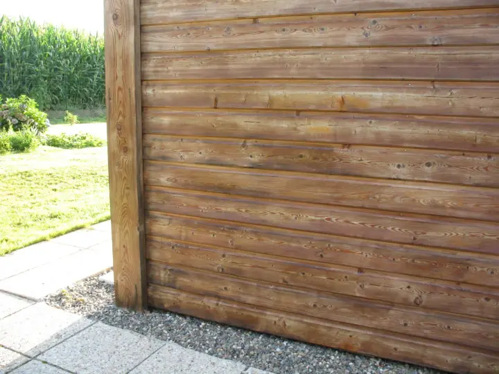 Bardage en bois de mélèze, traité pour l'extérieur, avec un poteau vertical. Le bois présente des nœuds et un grain prononcé.