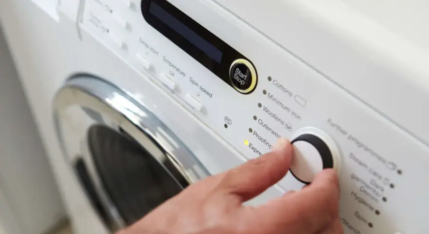 Main d'une personne réglant la température de lavage d'une couette sur un panneau de commande de machine à laver.