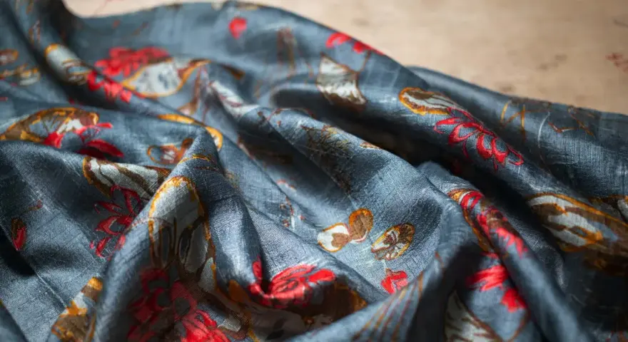 Tissu de soie bleu nuit avec un motif de fleurs rouges et de feuilles dorées. Une tache de gras sur soie, subtile, se fond dans le motif.
