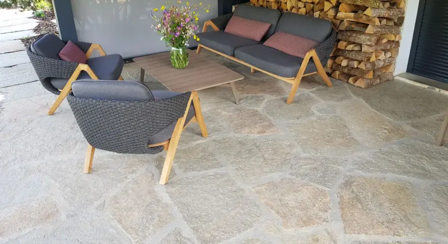 Terrasse en pierre naturelle extérieure, protégée par un imperméabilisant, avec mobilier de jardin confortable et un bouquet de fleurs sauvages.