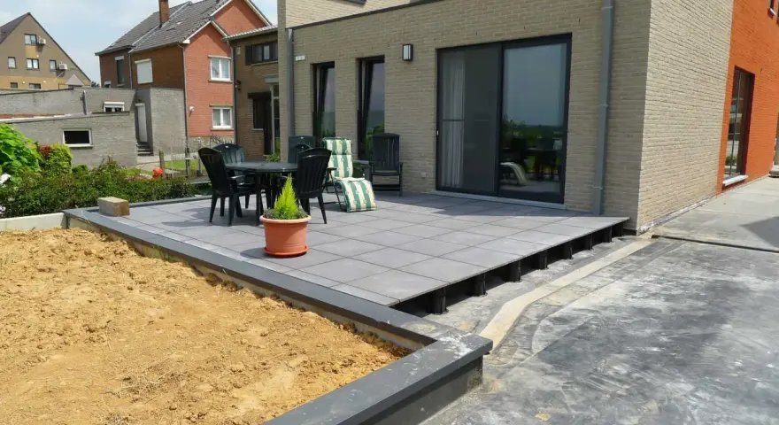 Une terrasse moderne avec un dallage gris sur plots, prête pour un couler dalle. Mobilier de jardin et végétation environnante.