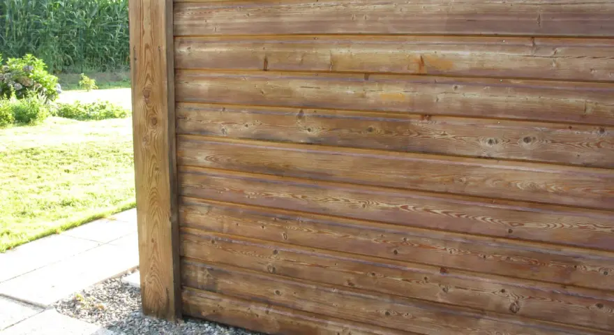 Bardage en bois de mélèze, traité pour l'extérieur, avec un poteau vertical. Le bois présente des nœuds et un grain prononcé.
