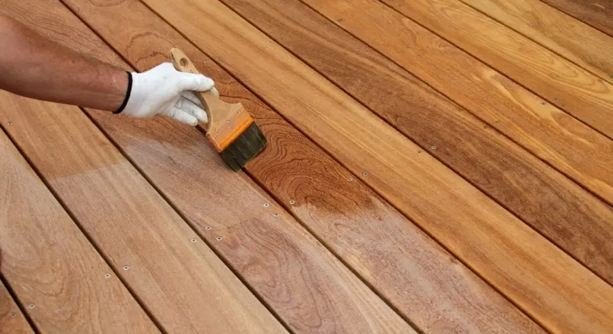 Application d'un produit protecteur sur un platelage en bois exotique, révélant sa beauté naturelle.