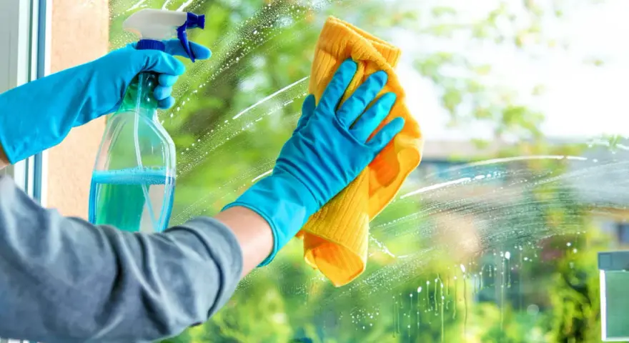 Mains gantées de bleu pulvérisent un produit pour nettoyer les vitres sans traces, puis essuient avec un chiffon jaune.