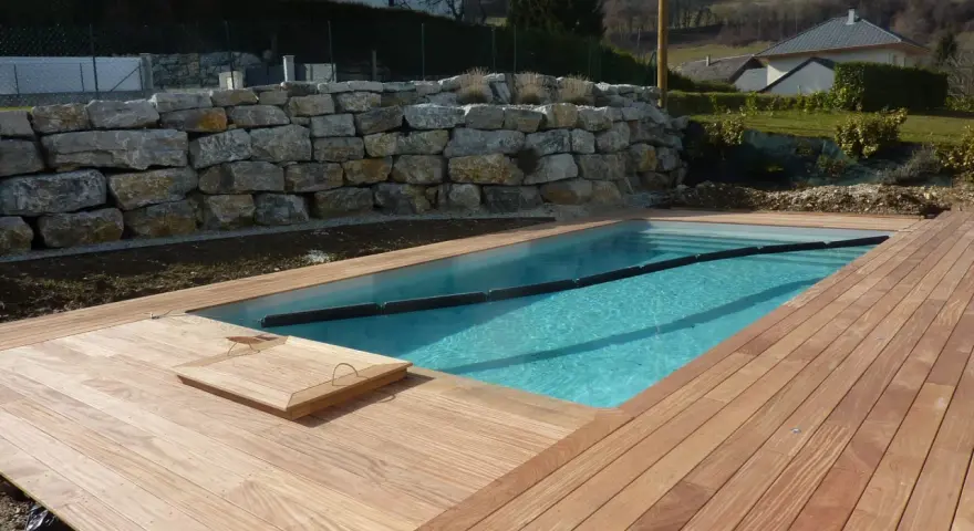 Piscine en bois avec terrasse en bois, mur de soutènement en pierre. Entretien piscine bois facile avec cette belle installation.