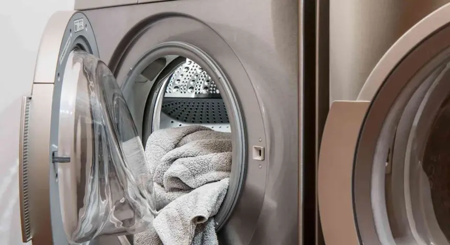 Machine à laver avec une porte ouverte, remplie de linge gris. Choisir la lessive la moins toxique pour un lavage sain.