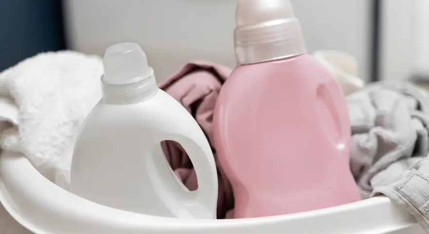 Deux bouteilles de lessive, une blanche et une rose, dans un panier avec du linge.