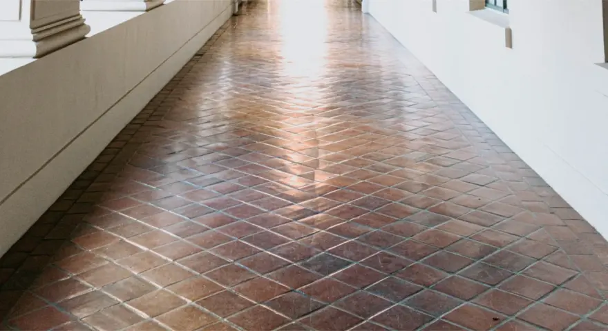 Un couloir avec un carrelage en terre cuite, dont la surface semble avoir été traitée pour vitrifier un carrelage, reflète la lumière.