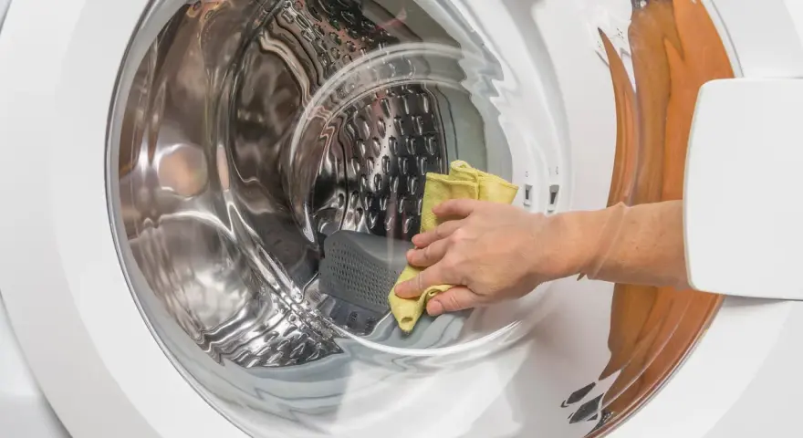 Main d'une personne utilisant un chiffon jaune pour nettoyer l'intérieur d'une machine à laver, une méthode naturelle pour nettoyer machine a laver vinaigre.