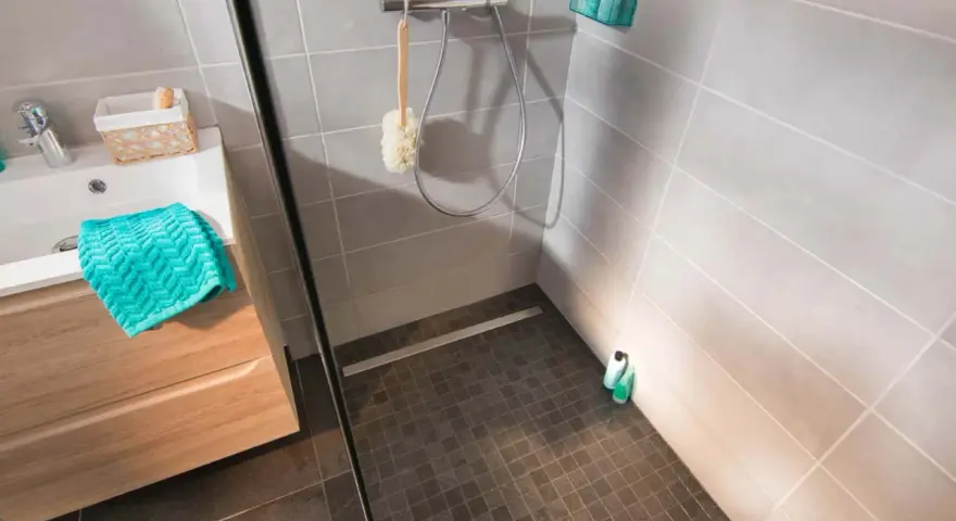 Sol de douche en galets sombres, contrastant avec le carrelage clair des murs. Une paroi vitrée sépare l'espace.