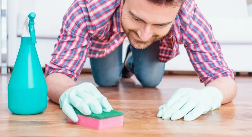 Un homme, muni de gants et d'une éponge, s'agenouille pour nettoyer une tache sur le parquet.