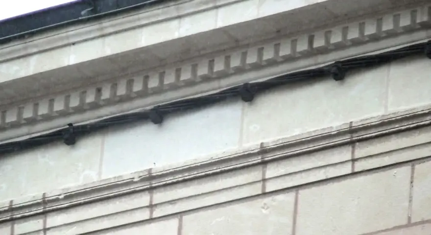 Détail d'une façade en tuffeau avec des câbles noirs fixés. L'image montre comment poncer du tuffeau pour restaurer sa surface.