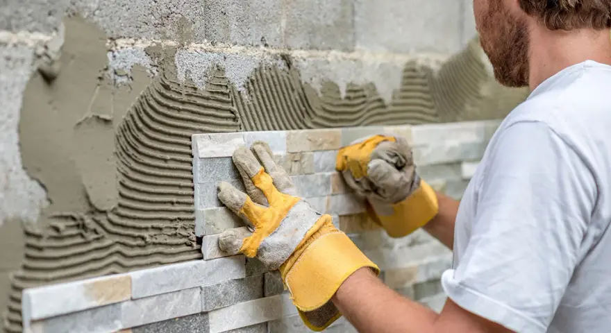 Pose de pierre de parement en quinconce. Un artisan pose des pierres naturelles sur un mur avec du mortier.
