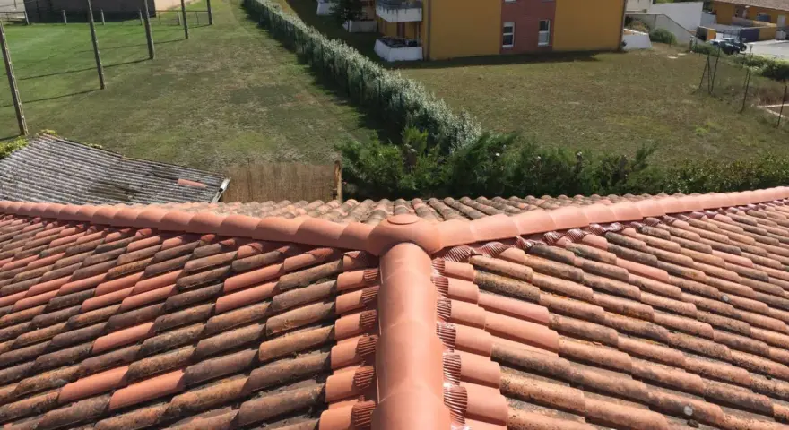 Vue aérienne d'un toit en tuiles rouges, avec des bâtiments et de la verdure en arrière-plan. Faut-il imperméabiliser les tuiles pour les protéger ?