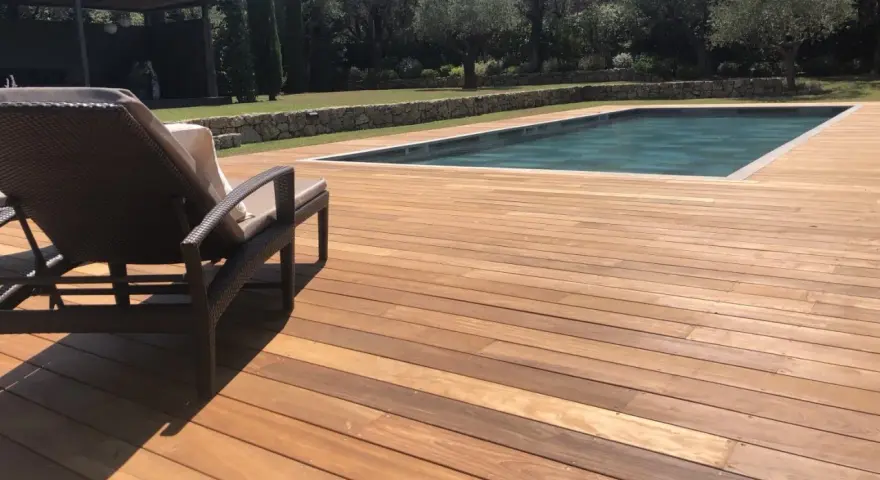 Terrasse en bois d'Ipe, baignée de soleil, avec une chaise longue invitant à la détente près de la piscine.