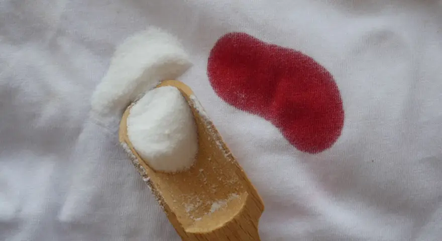 Poudre blanche sur tissu blanc à côté d'une tache rouge. Astuce pour savoir comment enlever des taches de sang sur du coton.