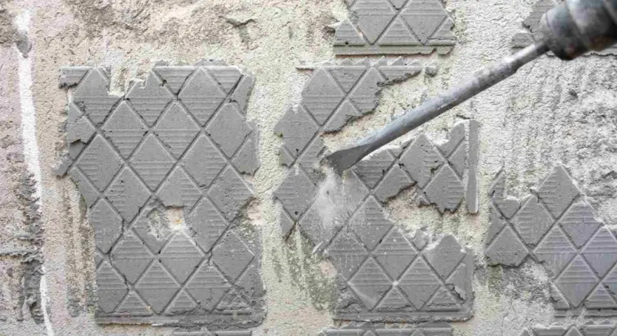Outil pneumatique en action pour enlever ciment colle sur carrelage. Poussière et débris volent.