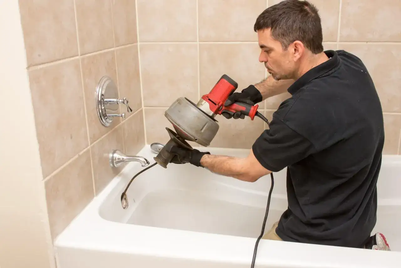 Plombier utilisant une tarière électrique pour déboucher une canalisation de baignoire.