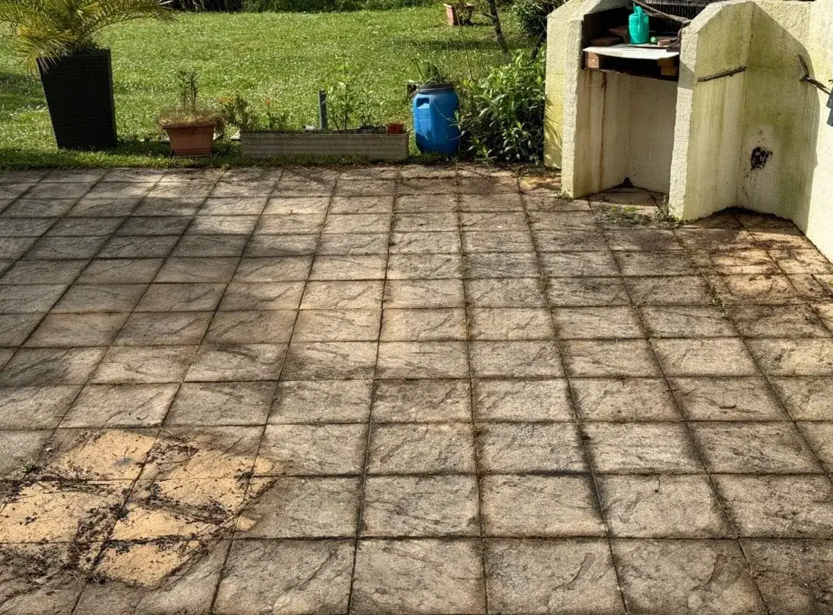 Terrasse en dalles grises, un peu sales, avec un barbecue en pierre à droite. Le nettoyage dalle terrasse s'impose.