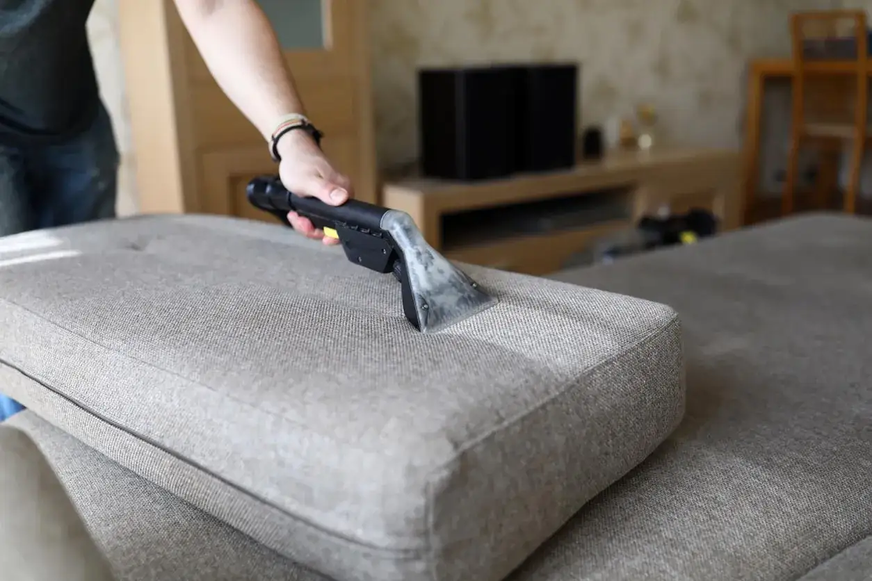 Main tenant utilise un appareil pour nettoyer canap&eacute; tissu vapeur. La vapeur p&eacute;n&egrave;tre les fibres pour un nettoyage en profondeur.