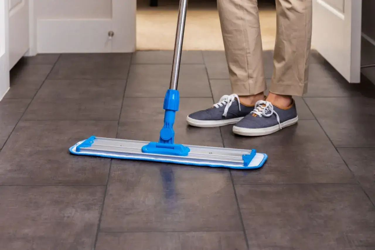 Une personne lave le carrelage sans trace avec une serpillère.