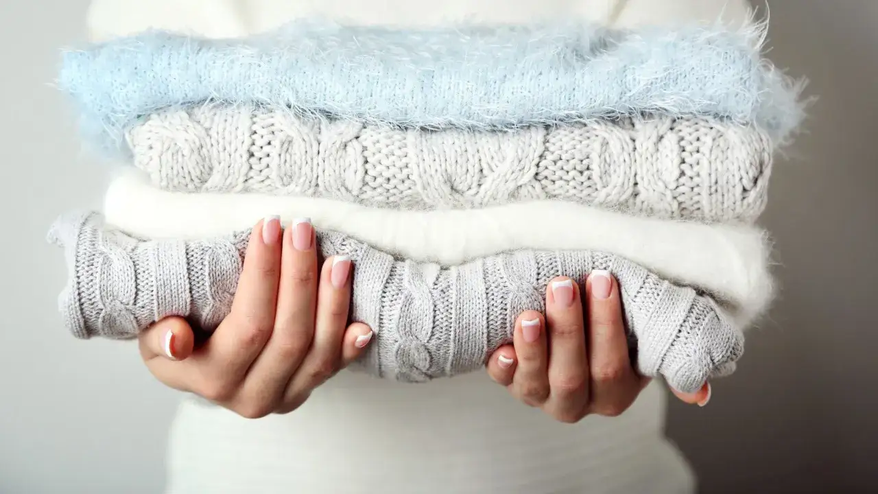 Mains soign&eacute;es tenant une pile de pulls douillets. Id&eacute;al pour savoir comment detacher un pull blanc et le garder comme neuf.
