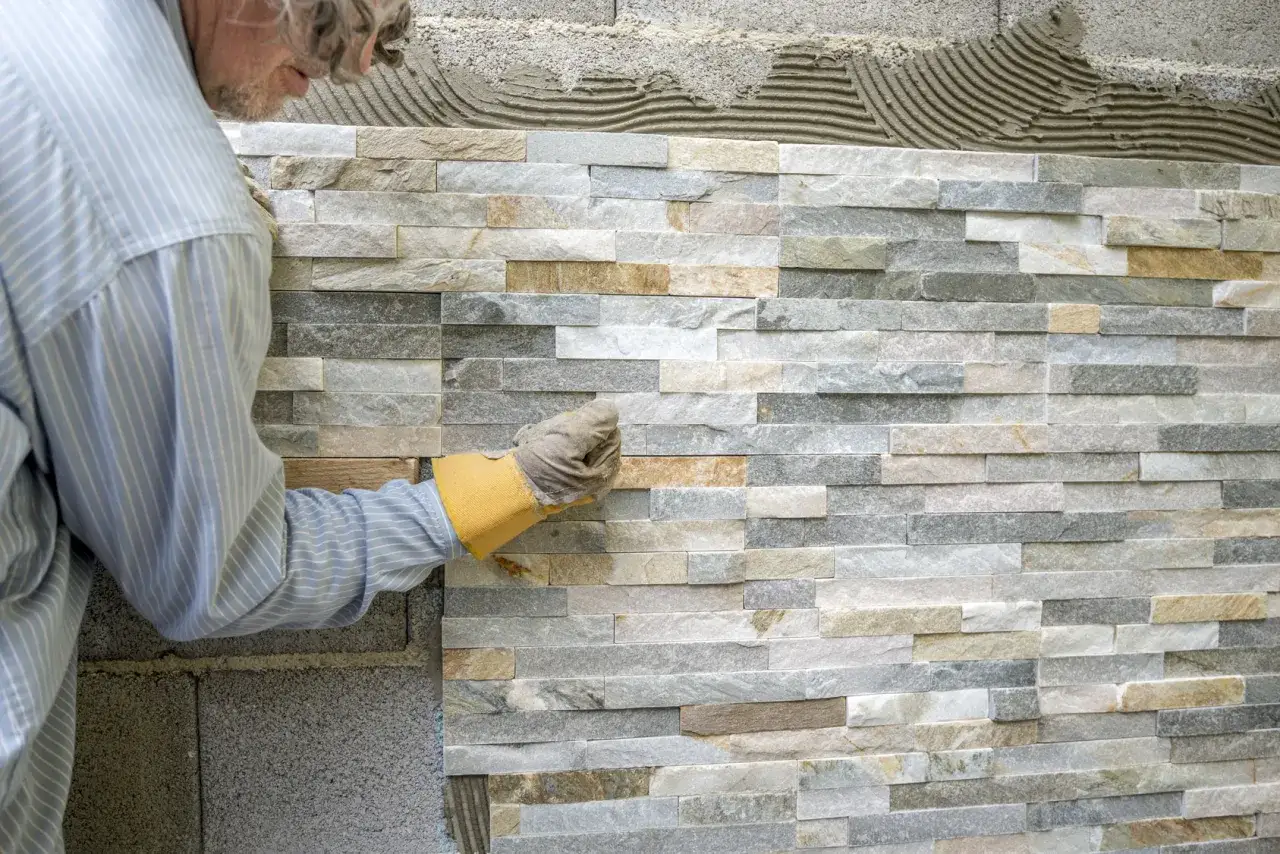 Un artisan pose des pierres de parement en quinconce sur un mur. La pose est minutieuse, créant un motif naturel et texturé.