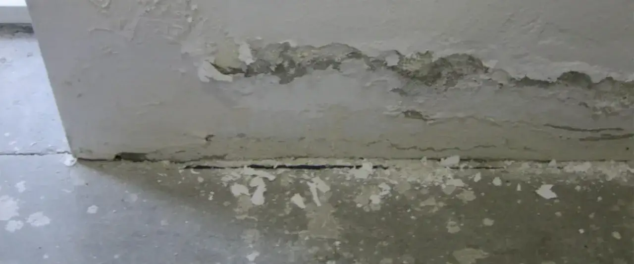Détérioration d'un mur avec efflorescence de salpêtre sur la dalle de béton.