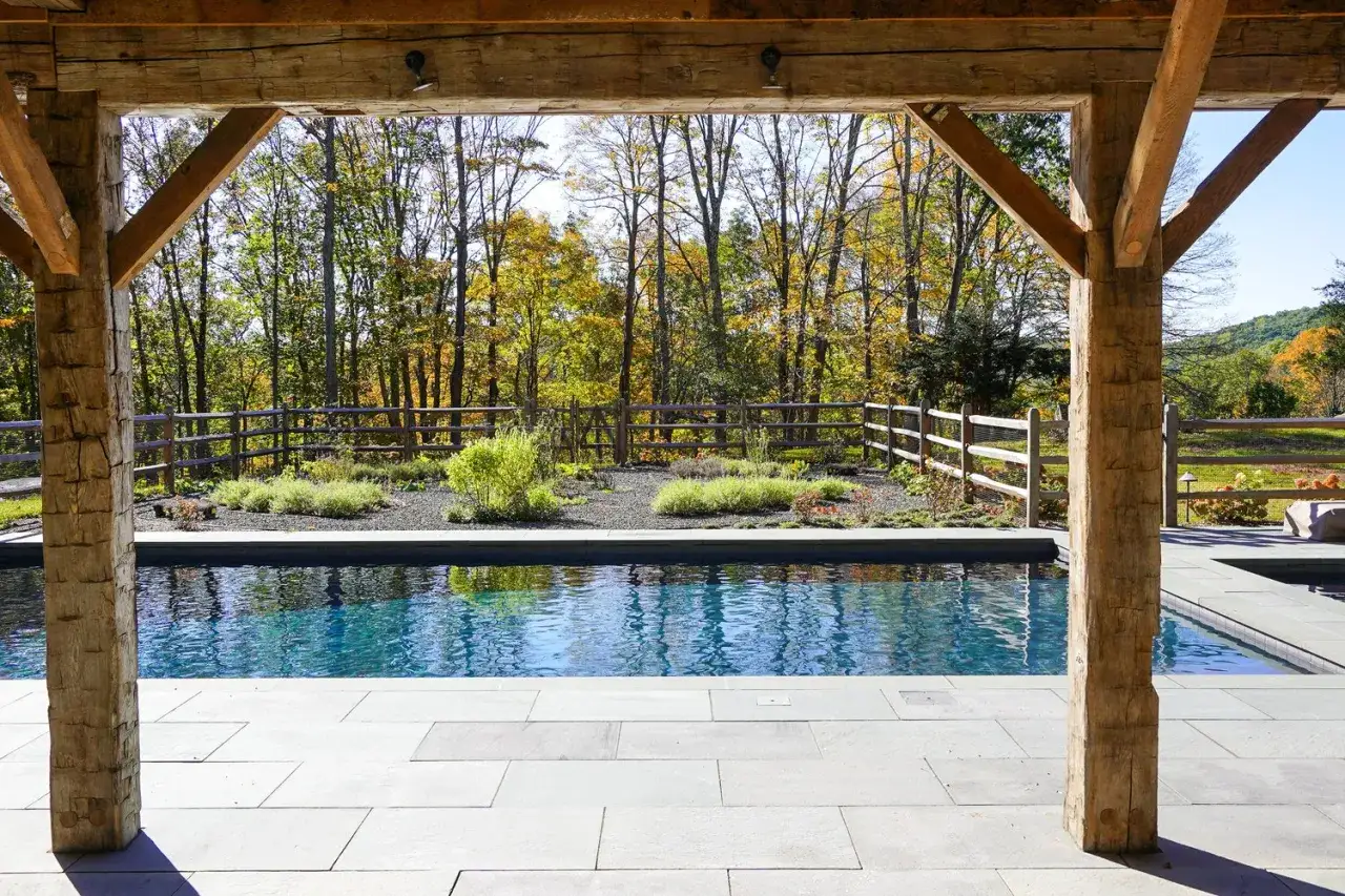 Piscine d'eau bleue sous une structure en bois rustique, entour&eacute;e de verdure et de feuillages d'automne. L'entretien piscine bois est essentiel pour pr&eacute;server cette beaut&eacute;.